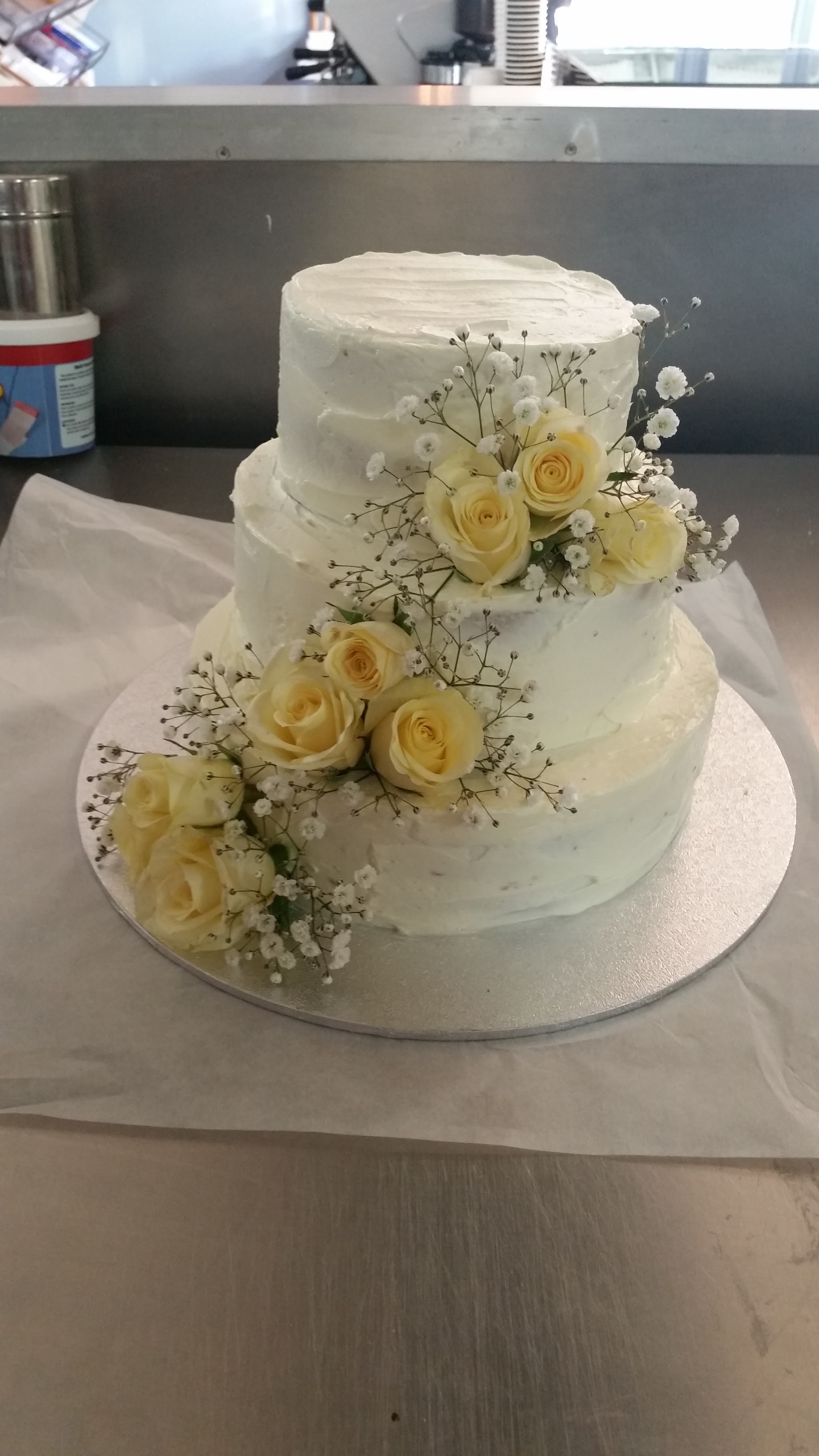 Two-tier white wedding cake decorated with yellow roses and baby's breath
